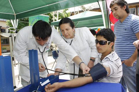 Un grupo de profesionales de la salud están tomando la presión arterial a un joven en un evento comunitario.