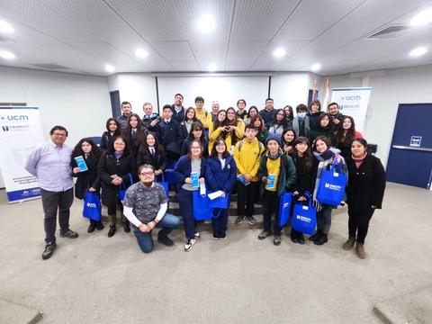 Un grupo de personas sonríe y posa en un evento, sosteniendo bolsas azules con el logo de la universidad.