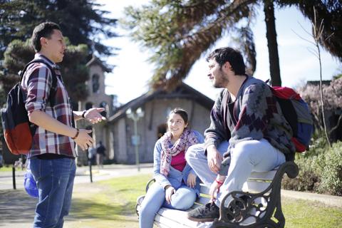 Un grupo de tres amigos conversando en un parque mientras disfrutan de un día soleado.