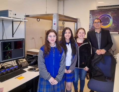 Un grupo de jóvenes y un adulto posan en un laboratorio con equipos científicos de fondo.