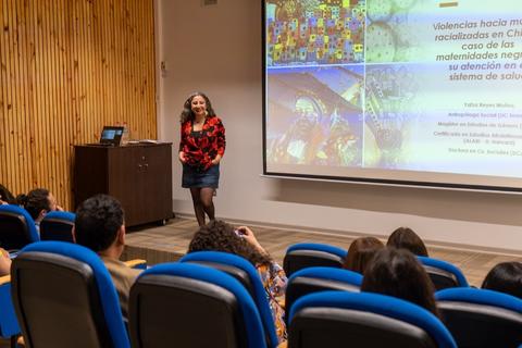 Una mujer presenta un tema sobre violencia y maternidades en un auditorio frente a un público sentado.
