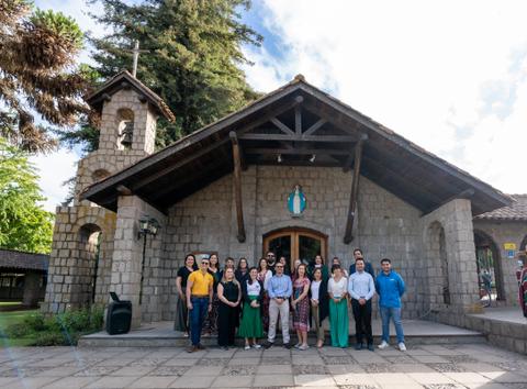 Grupo de personas posando frente a un edificio de piedra con un campanario en un día soleado.
