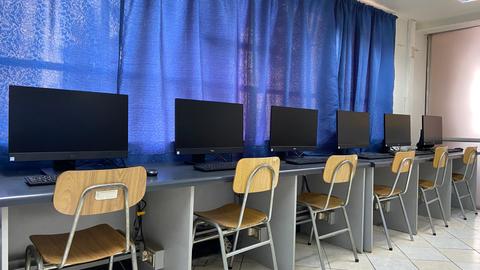 Una sala con varios computadores en fila frente a unas sillas vacías.