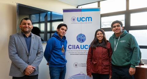 Un grupo de cuatro personas posando frente a un banner de la Universidad Católica del Maule.