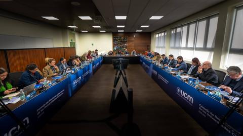 Una reunión formal en sala de conferencia con varias personas trabajando en sus laptops.