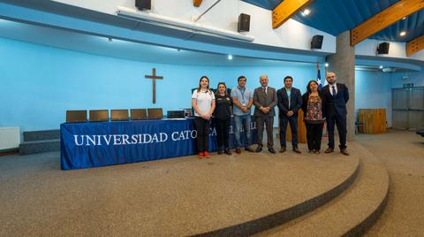 Un grupo de personas posando frente a un fondo de la universidad con una cruz en la pared.