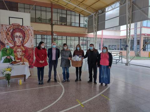 Un grupo de personas se encuentra en un gimnasio escolar durante un evento, con una decoración que incluye una imagen religiosa.