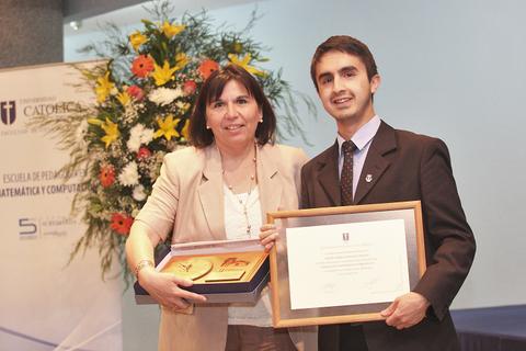Una mujer y un hombre posan juntos sosteniendo un premio en un evento de graduación en la Universidad Católica.