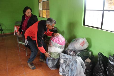 Una persona organiza bolsas de ropa en un espacio interior con paredes verdes.