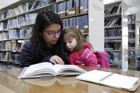 Una mujer y una niña pequeña leen juntas en una biblioteca.