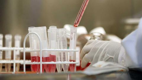 Un laboratorio muestra un técnico manipulando tubos de ensayo con líquidos de colores diferentes.