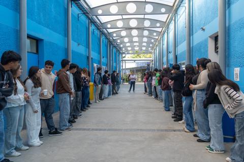 Un grupo de estudiantes está alineado en un pasillo azul, listos para participar en alguna actividad grupal.