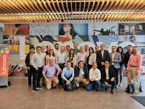 Un grupo de personas sonrientes posando frente a un mural colorido en las instalaciones de Lenovo.
