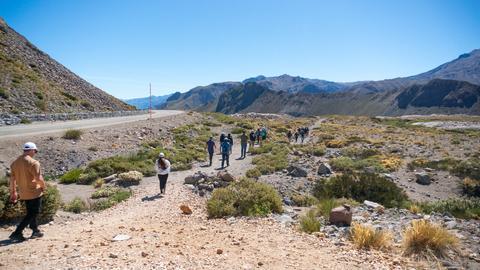 Un grupo de personas camina por un sendero en un paisaje montañoso bajo un cielo despejado.