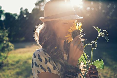 Una mujer sonriente huele un girasol mientras disfruta de un día soleado en el campo.