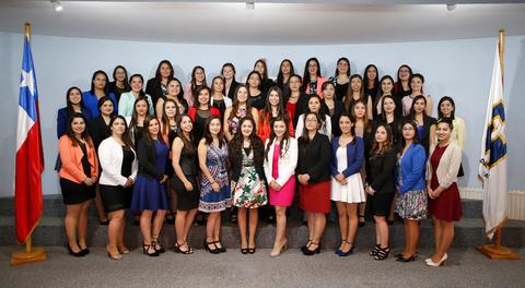 Un grupo de mujeres posando en una ceremonia formal con banderas chilenas de fondo.