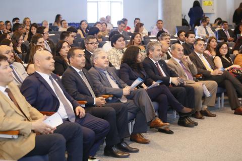 Un grupo de personas sentadas en un evento formal, prestando atención a la presentación.