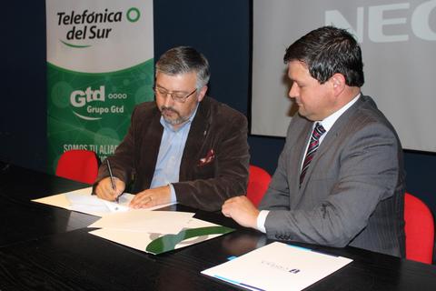 Dos personas firmando un documento en una mesa de negociación.