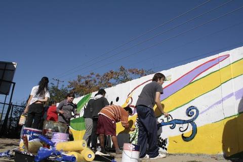 Un grupo de personas está pintando un mural colorido en una pared al aire libre.