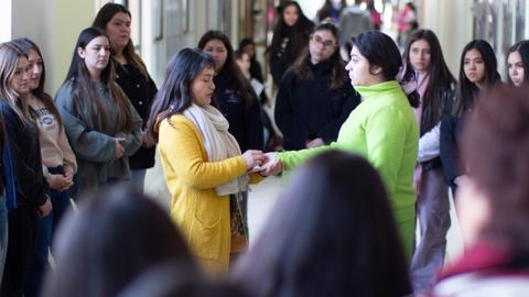 Un grupo de chicas observa a dos personas que se dan la mano en un pasillo.