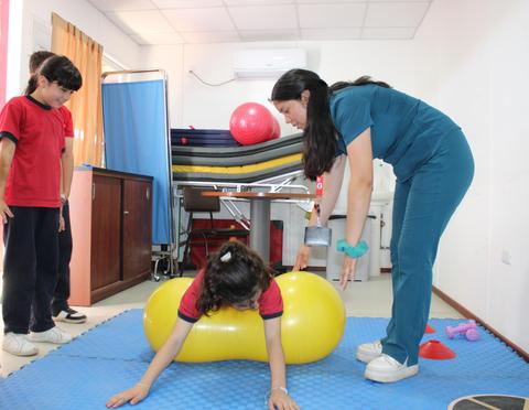 Una terapeuta ayuda a una niña a jugar con un objeto inflable en un entorno de rehabilitación.