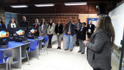 Un grupo de personas observa a una mujer que habla frente a varias computadoras en un aula.