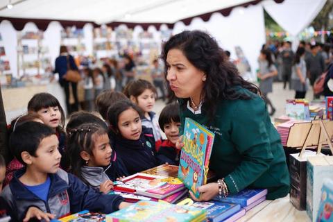 Una mujer interactúa con un grupo de niños en una feria de libros.