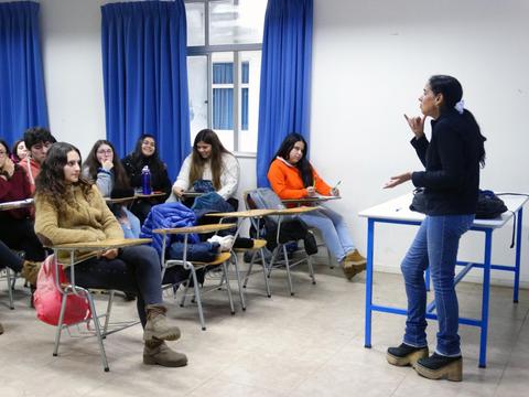 Un grupo de estudiantes escucha atentamente a una persona que está hablando frente a ellos en un aula.