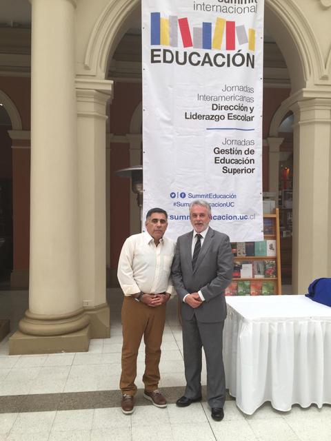 Dos hombres posan frente a un cartel que promueve jornadas sobre educación.