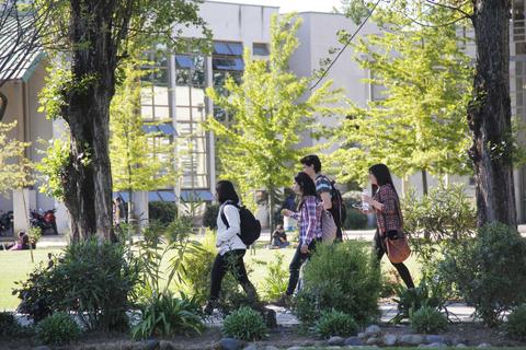 Un grupo de estudiantes camina por un campus universitario rodeado de árboles y plantas.