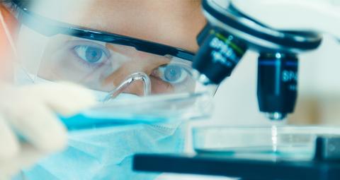 Un científico observa con atención a través de un microscopio mientras manipula una muestra en el laboratorio.