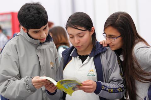 Tres adolescentes revisan un libro con interés en un ambiente escolar.