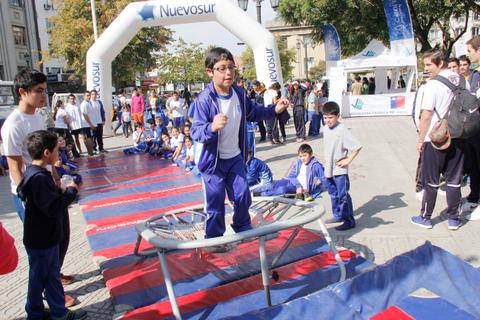 Un grupo de niños participa en una actividad recreativa al aire libre, con un niño saltando en una cama elástica frente a sus compañeros.