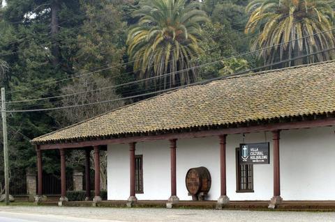 Edificio de estilo colonial con un barril y palmeras al fondo.