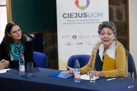 Una reunión donde dos mujeres discuten en una mesa con un fondo de un cartel del CIEJUS UCM.