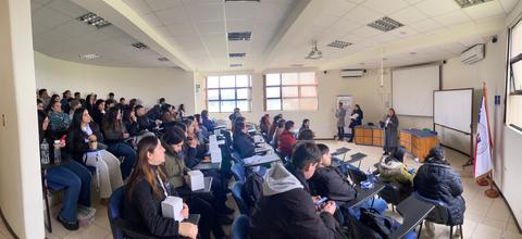 Una aula amplia con numerosos estudiantes atentos a una presentación frente a un proyector.