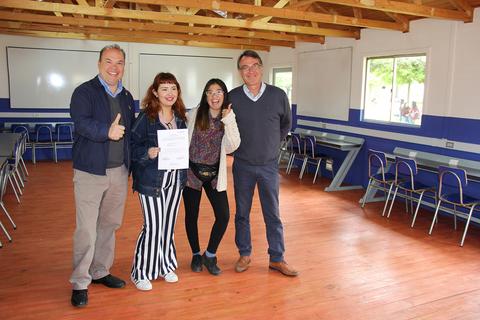 Un grupo de cuatro personas sonríen en una sala con escritorios y sillas.