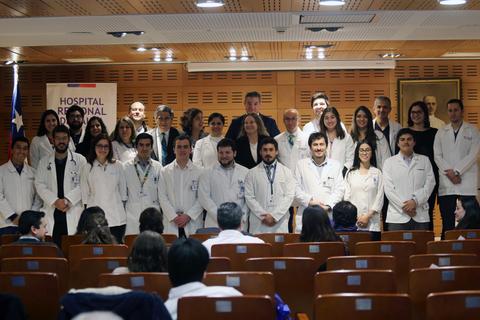 Un grupo de personas vestido con batas blancas se pose junto a un banner del Hospital Regional en un evento formal.