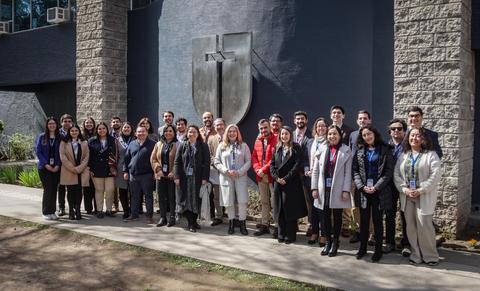 Un grupo de personas posando frente a un edificio con un escudo en la pared.