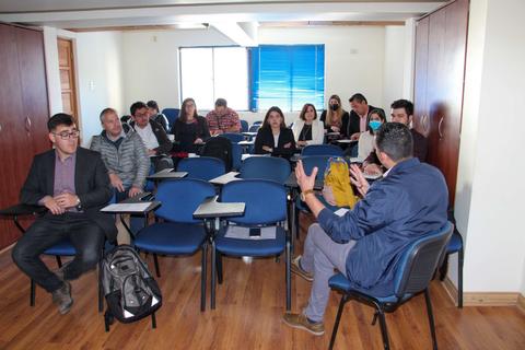 Un grupo de personas en una sala de capacitación, sentados en sillas frente a un presentador.