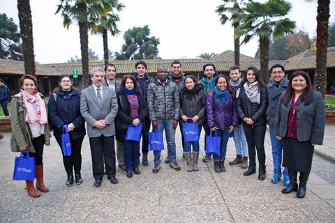 Un grupo de personas posando al aire libre, rodeados de palmeras, con mochilas azules en un ambiente social.