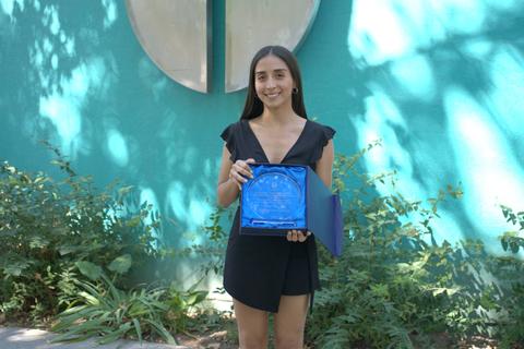 Una joven sostiene un premio sobre un fondo verde.