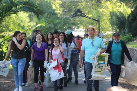 Un grupo de personas camina por un sendero en un parque, llevando bolsas de reciclaje.