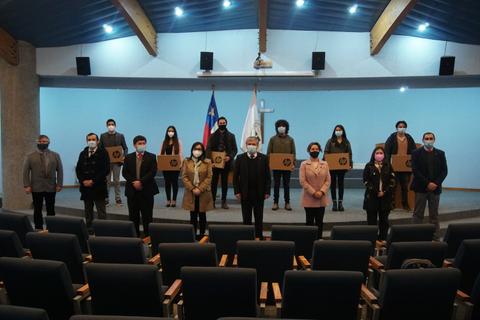 Un grupo de personas con mascarillas se encuentra en un auditorio, con banderas chilenas de fondo.
