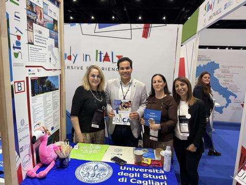 Un grupo de personas en un stand de una feria de educación mostrando información sobre estudiar en Italia.