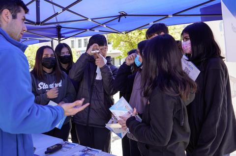 Un grupo de estudiantes interactúa con un presentador en un evento al aire libre.