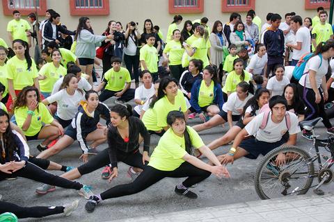 Un grupo de jóvenes vestidos con camisetas de colores brillantes realiza estiramientos en un evento al aire libre.