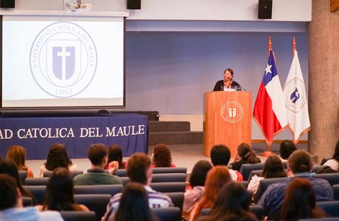 Una mujer presenta en un auditorio de la Universidad Católica del Maule frente a un grupo de estudiantes.