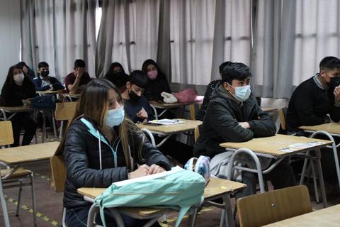 Un grupo de estudiantes en un aula, todos usando mascarillas y sentados en escritorios.