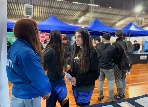 Un grupo de personas conversando en un evento bajo carpas azules.